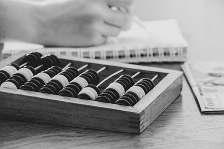 Old wooden abacus for counting money on a wooden table and a womans hand writes in a notebook and...