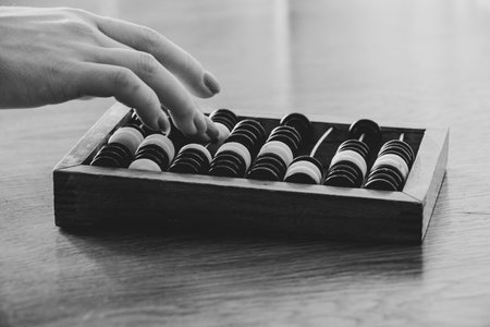 Old wooden abacus for counting money on a wooden table and a womans hand counts on the abacus, black and white photoの写真素材