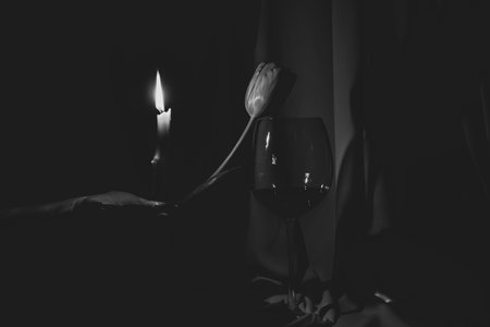 A glass of wine and one tulip and a candle in the hand in the dark, holiday and cultureの写真素材