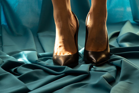 Female legs in black leather shoes with high heels on a dark blue fabricの写真素材
