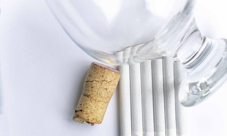 Empty wine glass and cork from wine and cigarettes on a white background, alcoholism and smokingの写真素材
