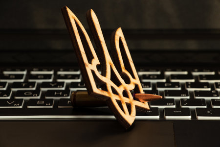 A bullet and a wooden coat of arms of Ukraine lie on a black laptop keyboardの写真素材