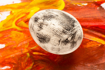 a white chicken egg painted in black paint lies on colored paperの写真素材