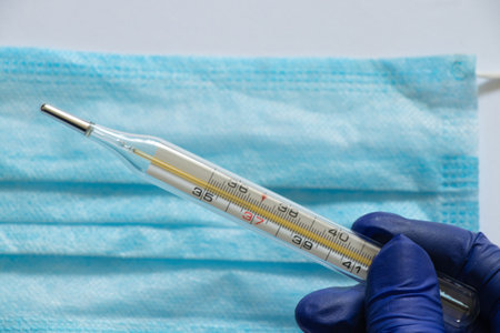 glass thermometer and hand in blue glove close-up on the background of the Medetsyn maskの写真素材