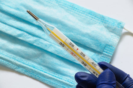 glass thermometer and hand in blue glove close-up on the background of the Medetsyn maskの写真素材