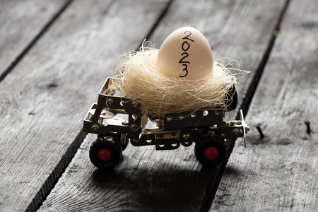 2023 is written on a chicken egg, which lies in a metal children's typewriter on a wooden board in...