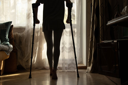 A little girl on crutches walks in the bedroom in her apartment near the window, rehabilitationの写真素材
