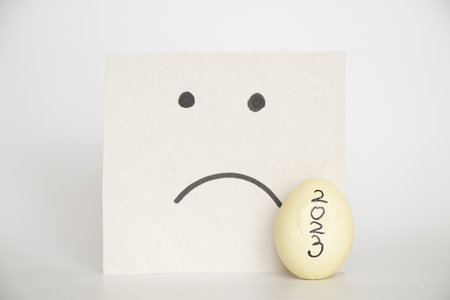 2023 written on a cracked white chicken egg and a card with a drawn sad smile on white, 2023 and a bad moodの写真素材
