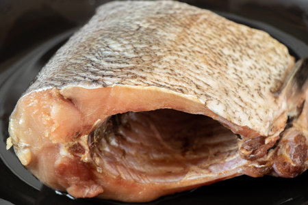 A raw piece of silver carp fish lies on a black plate