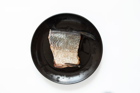 A raw piece of silver carp lies on a black plate on a white backgroundの写真素材
