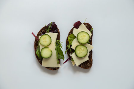 Vegetable sandwich with cheese and cucumbers and black bread with seeds on a white background, quick lunchの写真素材
