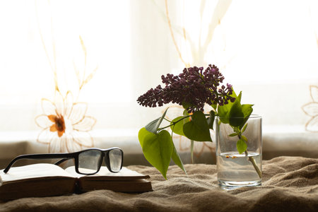 lilacs in a glass of water and an open old book on the table were taken to the windows close-upの写真素材