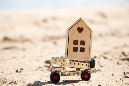 A car from a metal constructor transports a decorative small house on the sand, buying real estate,...