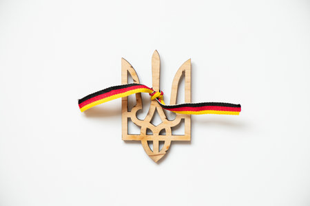 Wooden trident of Ukraine and the ribbon of the flag of Germany tied to a trident on a white background, friendship and unionの写真素材