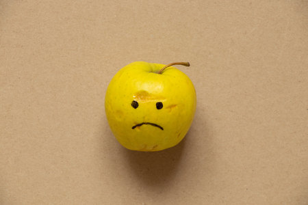 Green missing apple with a sad smile painted on brown paper, sadness and sadness, foodの写真素材