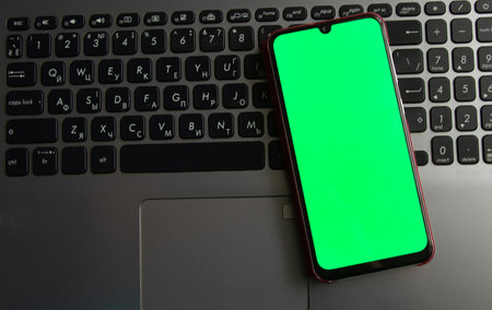 a laptop with a green screen and a touch phone is on the tableの写真素材