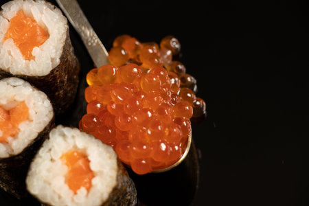 sushi with salmon and red caviar in a spoon on a black plate close-up