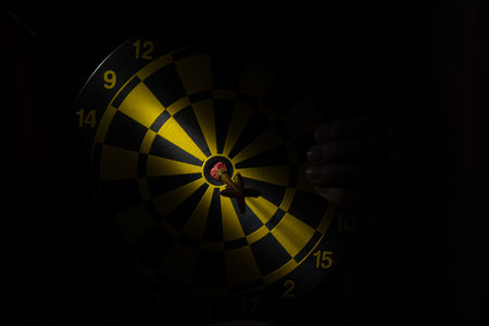 Darts and darts in the dark and a beam of light in the center close up and a woman's hand