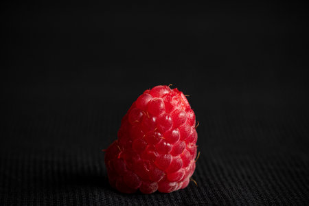 One raspberry lies on a black background close-up, fruit and berries