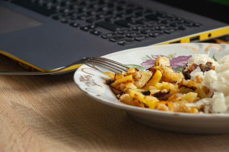 fried potatoes with cabbage in a plate near the laptop on the tableの写真素材