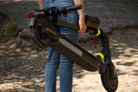 A girl holds an electric scooter in her hands in parks in Ukraine in the summer, urban electric...