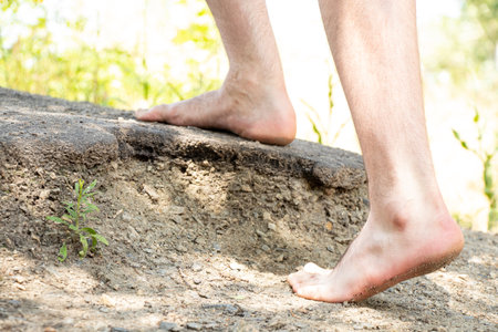 Men's bare feet climb the mountain to the top in the summer in the sun, go to the top, feet on the groundの写真素材