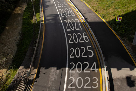 The years from 2023 to 2029 are written on the road with a turn to the left, the road goes in the mountains in the Carpathians and along the road there is a mountain river, Bukavel in Ukraineの写真素材