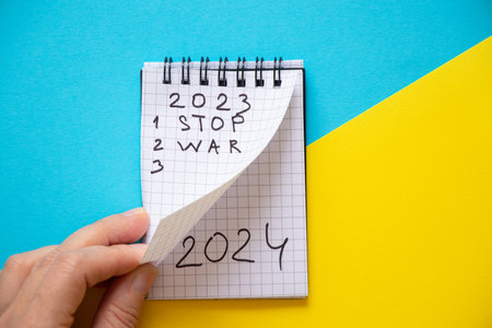 Notepad with the text 2023 and the text stop war and 2024 on the second page and the hand turns the page of the notebook against the background of the flag of Ukraine, stop war in 2023の写真素材