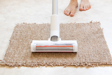 Vacuum cleaning on a beige rug on the floor and next to woman's leg, house cleaning, vacuuming an apartment, clean house and technologyの写真素材