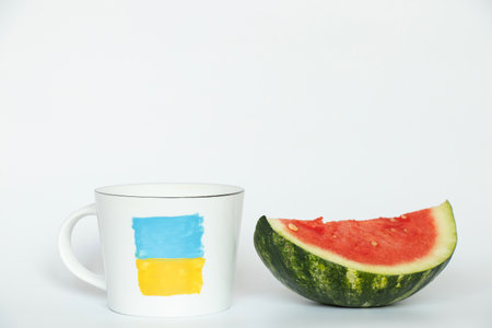 A cup with a drawn flag of Ukraine and a sliced watermelon next to it from the city of Kherson in Ukraine on a whiteの写真素材