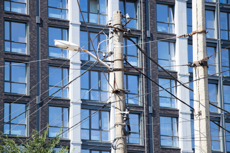 City pole with various cables and wires and street lighting on the background of the facade of a residential building in Ukraine in the summerの写真素材
