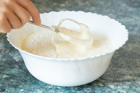 We beat the eggs with sugar on a mixer in a plate on the table in the kitchen, preparing the dough for the pieの写真素材