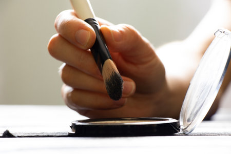 Woman's hand with a brush and powder in a plastic package on the table at home applies makeup, cosmetics and fashionの写真素材