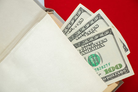 One hundred dollar bills lie in a book against the background of a red book, business and education