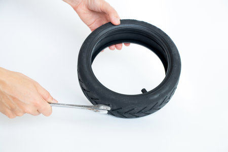 Tire of an electric scooter and a hand holds a wrench on a white background, replacement and repair of electric scooters, replacement of a wheel on a scooter, masterの写真素材