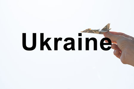 Airplane from one dollar in the hand of a girl in the sky over Ukraine and the text Ukraine on the background, freedom and lifeの写真素材