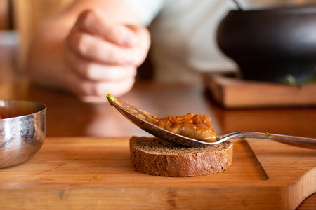 Marinated forest brown mushroom lies in a spoon on a piece of black bread on a board and a man in the background, lunch, mushrooms for lunch on the tableの写真素材