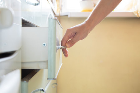 Woman's hand opens kitchen cabinet under sunlight, kitchen furniture at homeの写真素材