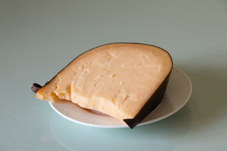 A piece of hard cheese lies on a plate on a glass table at home close-up, cheese for lunch, cheeseの写真素材