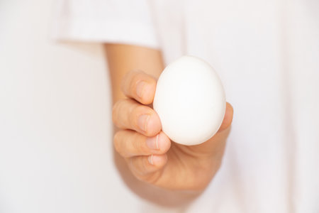 A woman's hand holds a white egg on a white background close-upの写真素材
