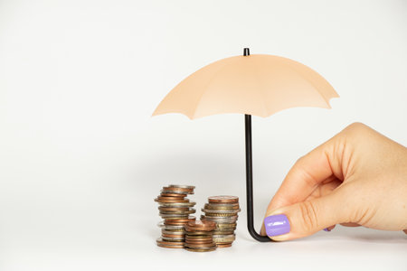 Stacks of coins under a small umbrella in a girl s hand on a white background, business and finance...