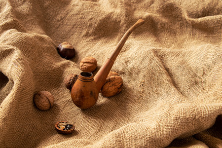 A smoking pipe lies on a brown burlap and nearby there are nuts and a chestnut close-upの写真素材