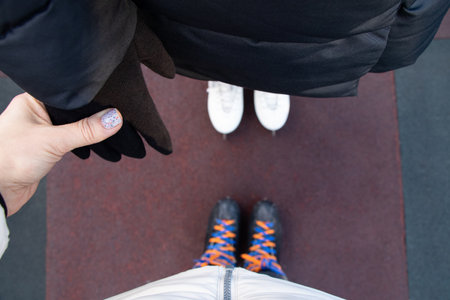 Two people holding hands while ice skating outdoors in winter, top down view of arms and legsの写真素材