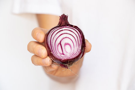 A woman's hand holds a cut purple onion on a white background close-upの写真素材