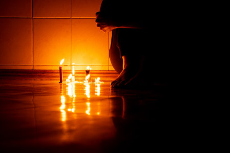 A girl sits on the floor in the dark with candles in an apartment in the dark without light in Ukraine, sitting on the floor alone in the dark, feetの写真素材