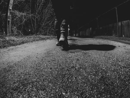 A girl walks along a wet winter road home in the dark, view from bottom to top, black and white photo, feet on the road in the darkの写真素材