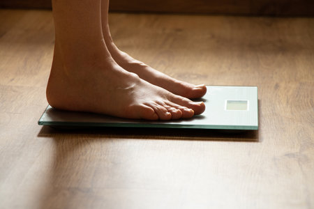 Woman's feet stand on bathroom scales at home on the floor in the light