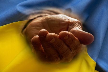The outstretched hand of an elderly woman against the background of the flag of Ukraineの写真素材