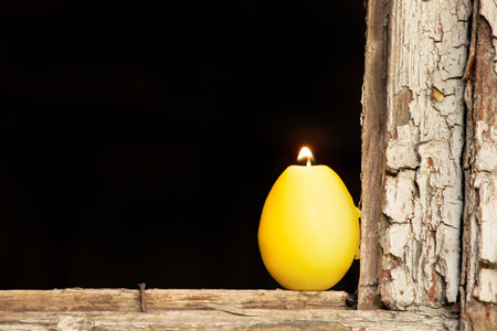 A burning candle in the shape of a yellow chicken egg stands on a broken window in Ukraine, Easter holidayの写真素材