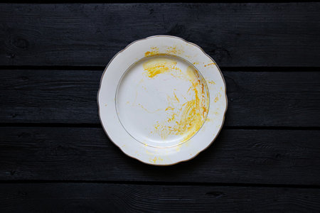 A white plate smeared with gold paint stands on a black boardの写真素材
